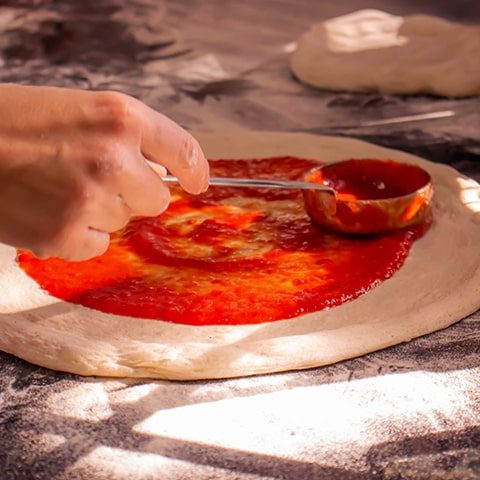 espalhando o molho de tomate com uma concha em cima de uma massa de pizza